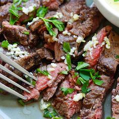 a plate full of steak with herbs on it and a fork in the bowl next to it