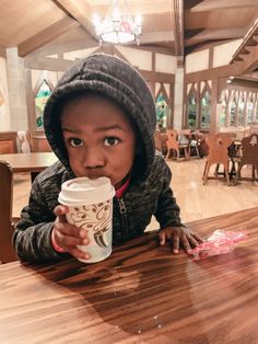 a young child sitting at a table with a coffee cup in front of her face