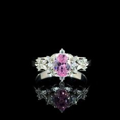 a pink and white diamond ring sitting on top of a black surface with reflection in the middle