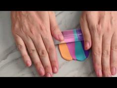 two hands holding an object on top of a marble surface with multicolored strips