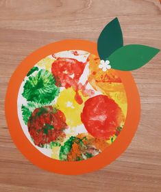 a paper plate with an orange and green leaf painted on the top, sitting on a wooden surface