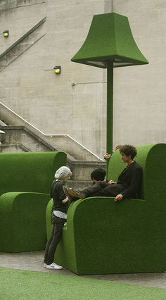 two people sitting on a green couch in front of a staircase and stairs, one person is looking at the child's phone