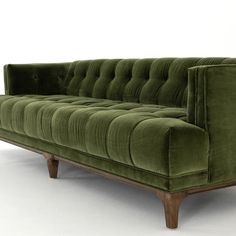 a green velvet couch with wooden legs on an isolated white flooring area in front of a wall