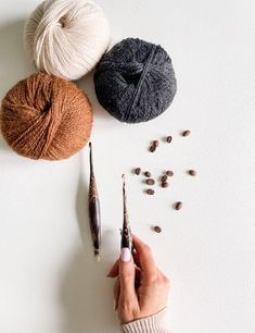 a person holding a crochet hook in front of three balls of yarn and seeds