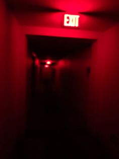 an exit sign is lit up in the dark with red light coming from behind it