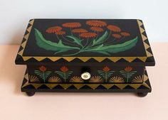 a black box with red flowers painted on the side and gold trimming around it