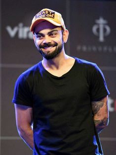 a man with a beard wearing a hat and black t - shirt smiles at the camera