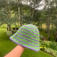 a crocheted green and purple hat sitting on top of a wooden stick in the grass