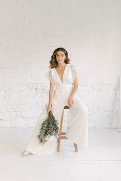 a woman is sitting on a chair holding a bouquet in her hand and wearing a white dress