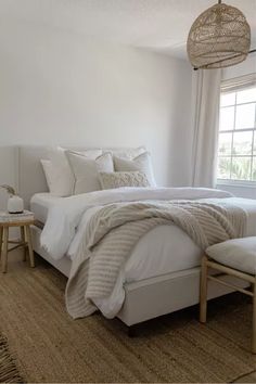 a bed with white linens and pillows in a bedroom next to a large window