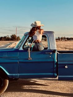 a woman sitting in the back of a blue pickup truck with her hat on top