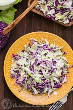 a yellow plate filled with coleslaw on top of a wooden table next to two serving utensils