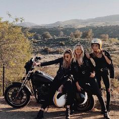 three women are posing for a photo while sitting on a motorcycle in the middle of nowhere