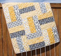 a yellow and gray quilt hanging on a wooden fence with blue sky in the background