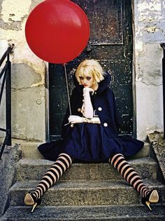 a woman sitting on steps with a red balloon in front of her face and legs