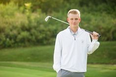 a young man holding a golf club in his right hand and wearing a white shirt