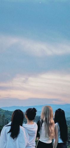 three girls standing on top of a hill looking at the sky