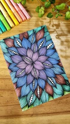 a notebook with colored pencils next to it on a wooden table and some flowers