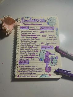 a spiral notebook with writing on it next to two purple pens and a seashell