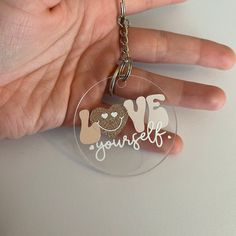 a hand holding a keychain with the words love yourself on it and a teddy bear