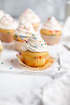 cupcakes with white frosting and sprinkles are on a napkin