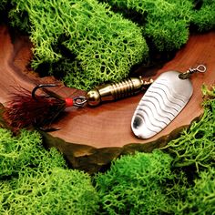 a fishing lure sitting on top of a piece of wood next to some green plants