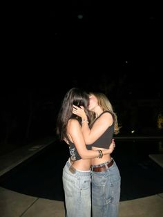 two women standing next to each other in front of a pool at night with their arms around each other