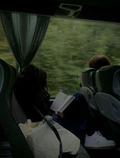 two people sitting on a bus looking out the window at grass and trees in the distance