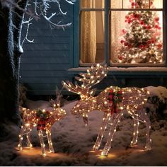 two lighted reindeers in front of a house with a christmas tree and window behind them