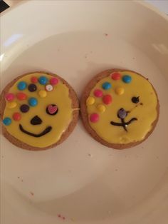 two decorated cookies on a plate with sprinkles in the shape of faces