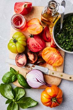 tomatoes, basil, and other vegetables on a cutting board next to a bowl of pesto