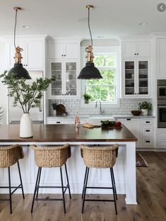 a kitchen with white cabinets and wooden counter tops, two black pendant lights hanging over the island