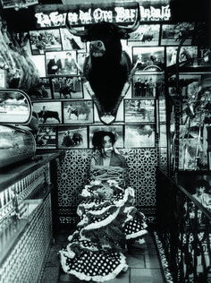 black and white photograph of a woman sitting in a booth with pictures on the wall