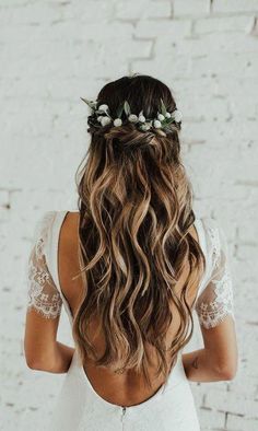 a woman with long hair wearing a white dress and flowers in her hair, standing against a brick wall