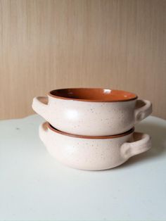 two white and brown bowls sitting on top of a table next to eachother