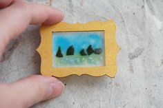 a hand holding a miniature photo with trees in the background on a piece of wood