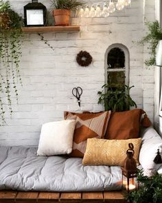 a couch with pillows and plants on it in front of a white brick wall filled with potted plants