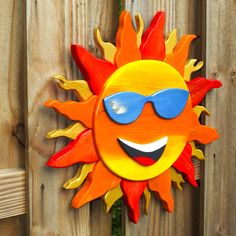 a wooden sun with sunglasses on it's face is hanging on a wood fence