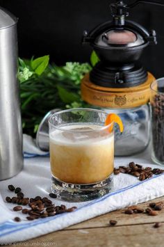 a glass filled with liquid sitting on top of a table next to some coffee beans