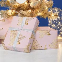 two wrapped presents under a christmas tree with gold ornaments and lights on the blue background