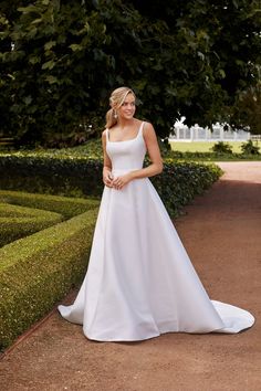 a woman in a white wedding dress standing on a path next to hedges and trees