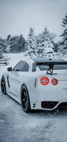 a white sports car parked in the snow with its hood up and tail lights on