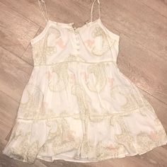 A Off-White Sundress With Tan And Pink Details Beachy Sleeveless Beige Dress, White Mini Dress For Beach Season And Garden Party, White Mini Dress For Garden Party And Beach Season, Beige Floral Print Sundress For The Beach, Beige Floral Print Sundress For Beach, Beige Floral Sundress For The Beach, Beige Floral Sundress For Beach, Beige Sundress For Brunch During Beach Season, Cream Dress For Summer Garden Party