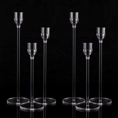 four clear glass candlesticks are lined up on a black surface with one candle holder in the middle