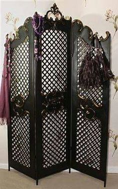 an ornate black room divider with flowers and tassels on the top, in front of a white wall