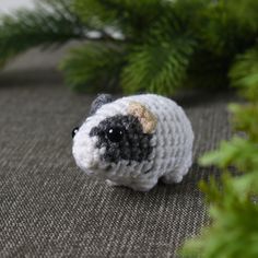 a small crocheted sheep sitting on top of a carpet next to green plants