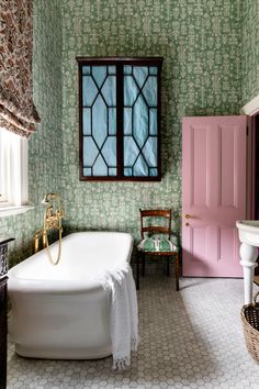 a bath tub sitting next to a pink door in a green and white bathroom with floral wallpaper