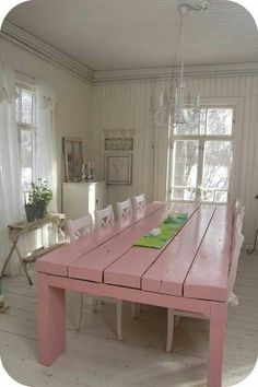 a pink table with white chairs sits in the middle of a room next to two windows