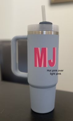 a cup with a straw in it sitting on a table next to a mug that says, mj hot pink over light pink