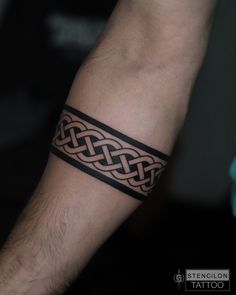 a man with a tattoo on his arm wearing a black leather wristband that has an intertwined design